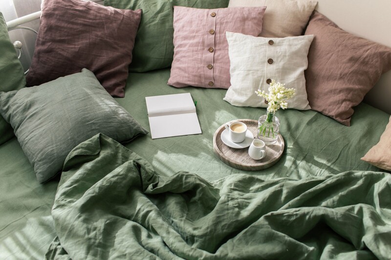 Several linen pillows are stacked up on a bed with green bedding. Green is an interior design trend to watch for in 2022. 