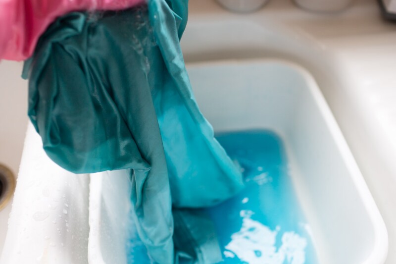 Step five in the ombre tie-dye technique. A hand wearing a pink glove rinses out dye water from the pillowcases. 