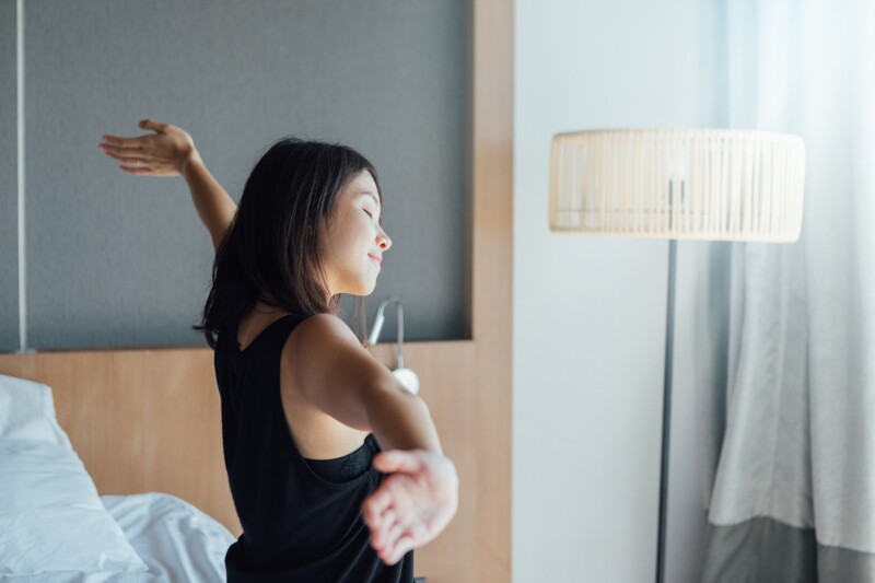 Woman stretching her arms and smiling on the side of her bed, greeting the morning. 