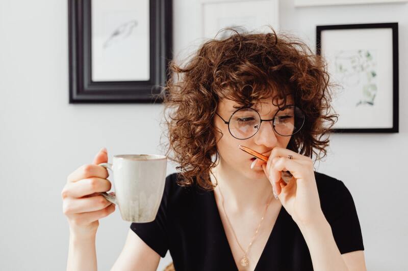 Person holding a cup of coffee while working on a task after waking up early in the morning