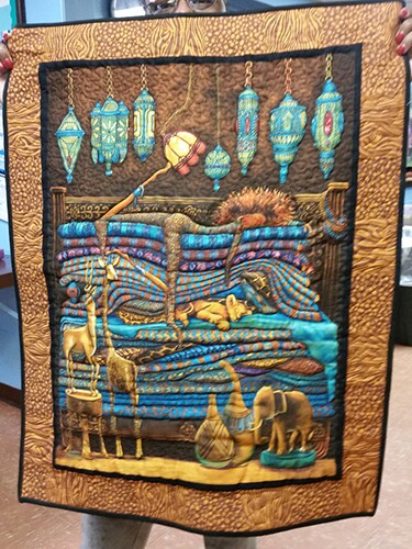 A woman holds up a tapestry quilt with an animal motif. This is a quilt by African American quilt artists, filled with culture, history, and art. 