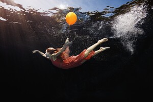 woman in a red dress swimming holding an orange balloon