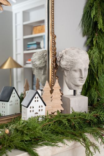 Holiday décor ideas for the guest bedroom. Garland and seasonal figurines are arranged in front of a gold-trimmed mirror. 