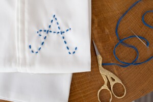 A standard white pillowcase embroidered with an A initial, in blue thread. A pair of scissors and a threaded needle sit beside the pillowcase. Use this guide to learn 澳门一肖一码一必中一肖✪how to embroider an initial on a pillowcase, a unique element for your bedroom decor. 