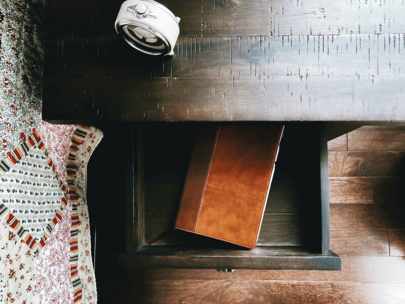 A wooden nightstand with a journal inside the drawer