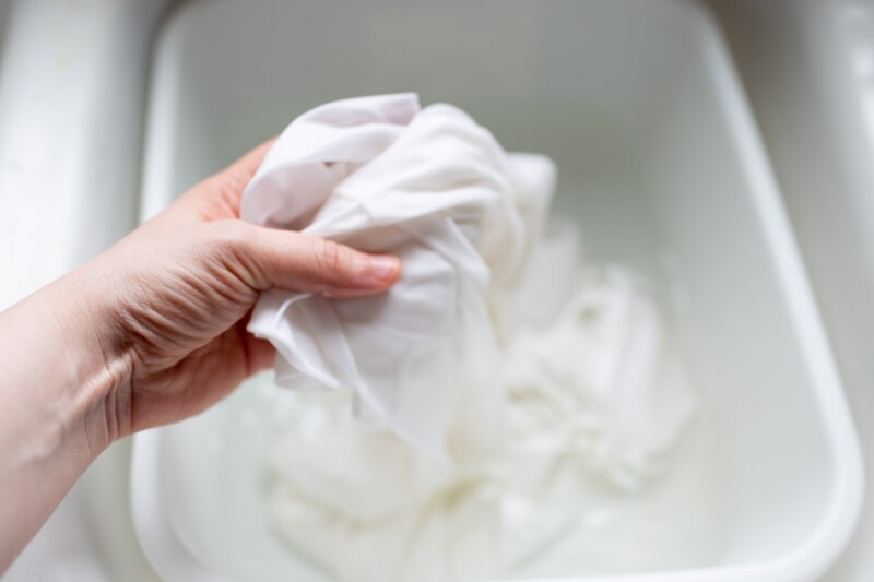 Step one to the DIY ombre tie-dye technique for pillowcases. A hand holds up a wet white linen out of a wash basin to prep for tie-dyeing. 